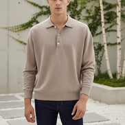 Man wearing a beige long-sleeve polo shirt and dark jeans on a plain background