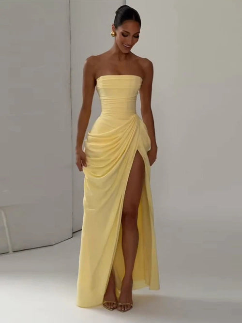 Woman wearing a yellow strapless gown with a high slit on a plain background