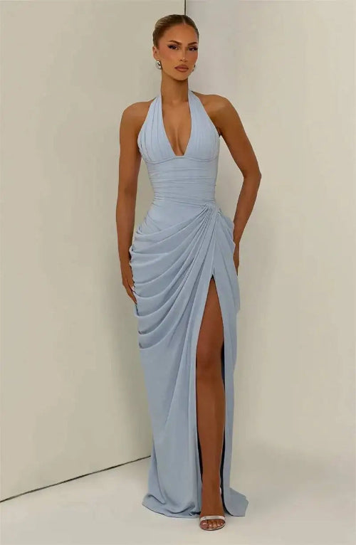 A woman modeling a light blue halter-neck maxi dress with a deep V-neckline, draped skirt details, and a high thigh slit, 