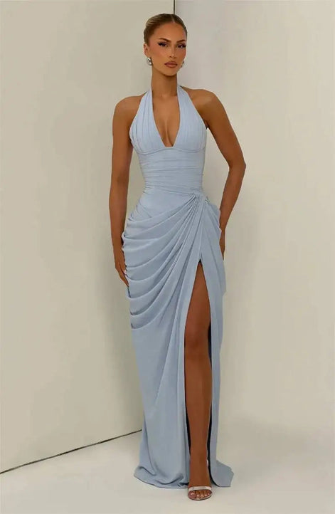 A woman modeling a light blue halter-neck maxi dress with a deep V-neckline, draped skirt details, and a high thigh slit, 
