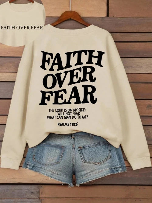 Beige sweatshirt with 'Faith Over Fear' text on a wooden background