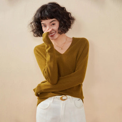 Woman wearing a mustard yellow sweater and white pants against a beige background