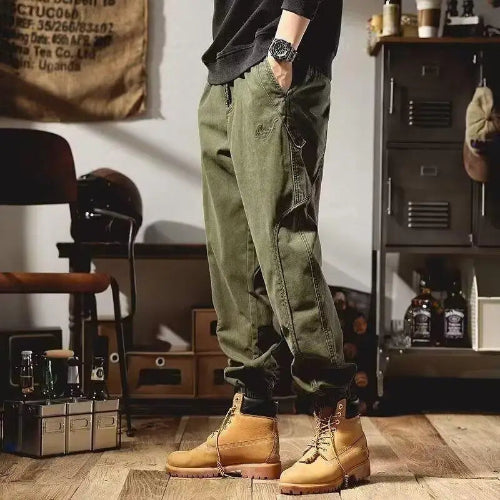 Front-angle view of a model wearing olive green loose-fit cargo pants with curved side seams and gathered ankle cuffs, paired with tan lace-up boots.