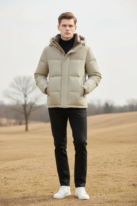 A man wearing a light beige hooded puffer jacket with a brown inner hood lining over a black turtleneck. Three feature callout graphics on the left highlight down insulation, warm thickness, and soft fluffiness.