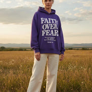 Purple hoodie with 'Faith Over Fear' text on a wooden surface