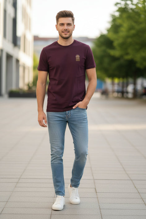 Maroon t-shirt with a small logo on a hanger against a light background