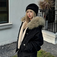 Person wearing a black coat with a fur-lined hood outdoors.