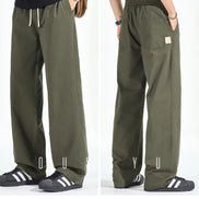 Front and back views of a model wearing army green loose-fit straight-leg pants, showing a white drawstring, elastic waistband, side pockets, and back patch pockets.