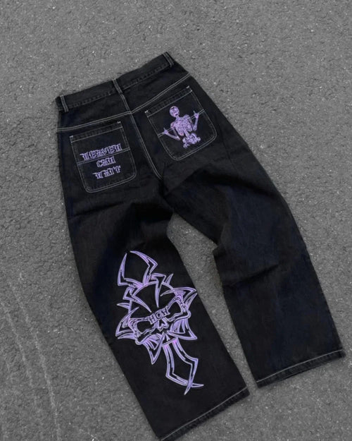 Back view of black wide-leg jeans laid flat, featuring purple lettering and a skeleton graphic on the back pockets and a large purple cross-style design on one leg.