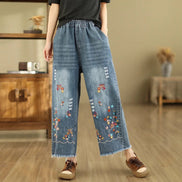 Person wearing blue denim pants with floral embroidery in a room setting.