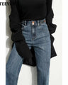 A model wearing high-waisted, wide-leg blue denim jeans with a black long-sleeve 