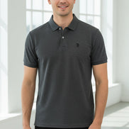 Gray polo shirt with a red logo held by a hand, with other colored shirts hanging in the background.