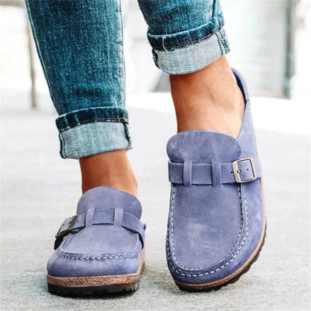 Blue suede loafers with buckles worn with rolled-up jeans on a light background