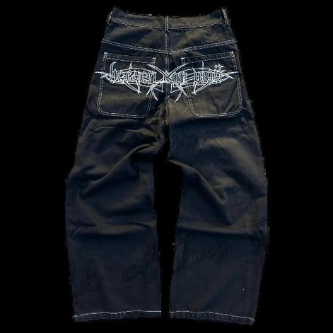 Back view of black wide-leg jeans laid flat, featuring white contrast stitching and a large white gothic lettering graphic across both back pockets.
