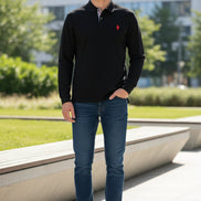 Black long-sleeve polo shirt with a red logo on a rack in a store.