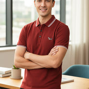 Red polo shirt with a small dog emblem held by a hand, on a rack of similar shirts.