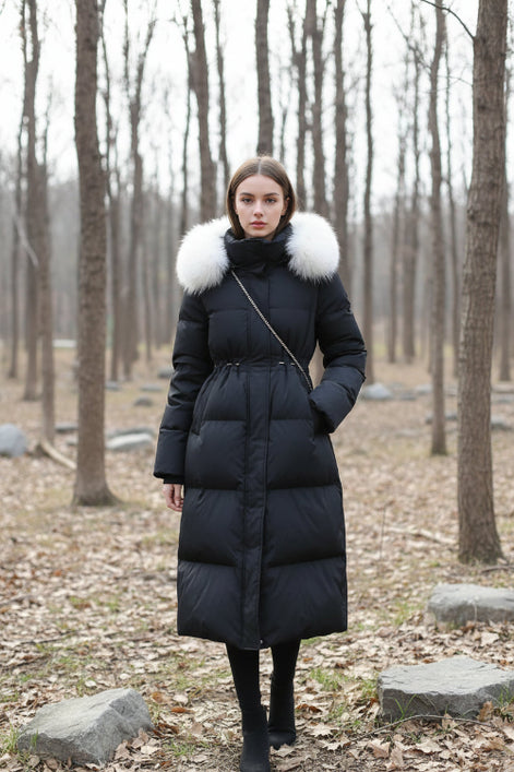 A person takes a mirror selfie wearing a long black puffer coat with a large light beige fur-trimmed collar. 