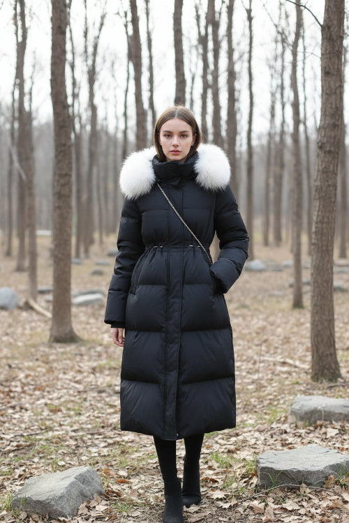 A person takes a mirror selfie wearing a long black puffer coat with a large light beige fur-trimmed collar. 