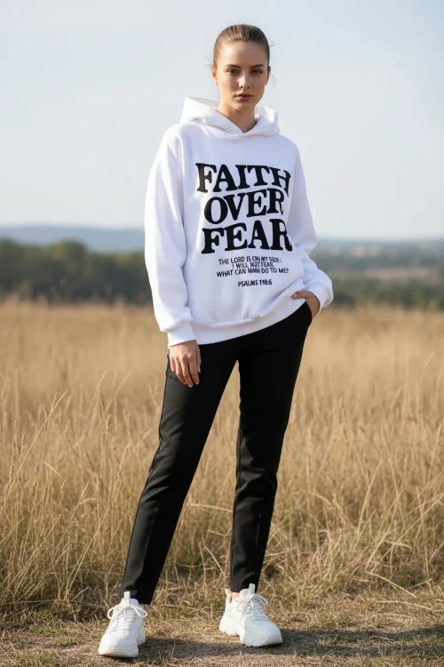 White hoodie with 'Faith Over Fear' text on a concrete surface with sneakers and a plant.