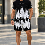A man wearing a matching black and white abstract print t-shirt and shorts set, standing outdoors on a paved walkway.