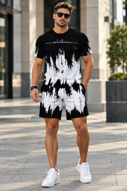 A man wearing a matching black and white abstract print t-shirt and shorts set, standing outdoors on a paved walkway.