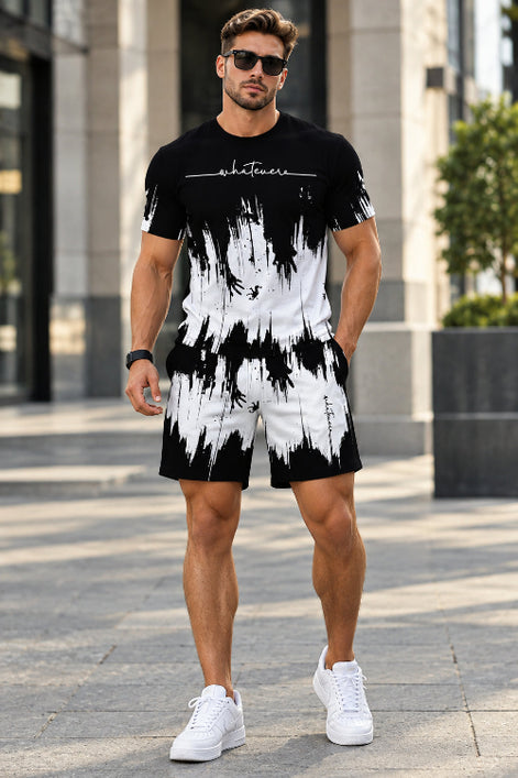 A man wearing a matching black and white abstract print t-shirt and shorts set, standing outdoors on a paved walkway.