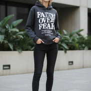 Dark gray hoodie with 'Faith Over Fear' text on a wooden surface with shoes and a plant.