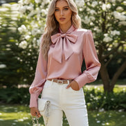 Pink satin blouse with a large bow tie worn by a person, sitting on a white couch.