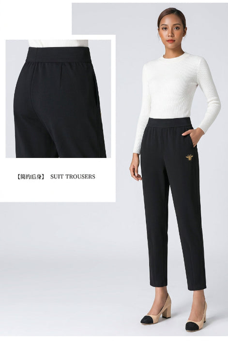 Black high-waisted slim-fit suit trousers shown on a model, with a close-up inset of the waistband and a small gold embroidered bee detail 
