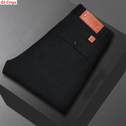 Black men's jeans folded neatly on a dark gray platform, showing the back pocket, button closure, and orange-brown leather brand patch. The brand name QJ Cinga 