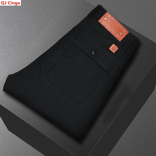 Black men's jeans folded neatly on a dark gray platform, showing the back pocket, button closure, and orange-brown leather brand patch. The brand name QJ Cinga 