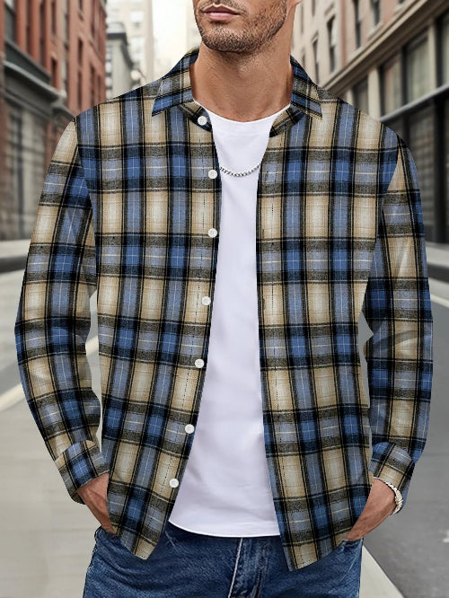 A man wearing a blue, beige, and black plaid button-down shirt over a white t-shirt and blue jeans, standing on a city street.
