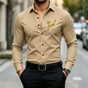 A man wearing a beige long-sleeve button-up shirt with a gold embroidered horse and the words 'Success at first try' on the left chest, 