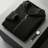 Folded black sweater with a watch on a gray surface
