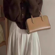 A person taking a mirror selfie wearing a dark brown ribbed knit cardigan, a long cream-colored pleated skirt, and carrying a structured tan leather handbag.
