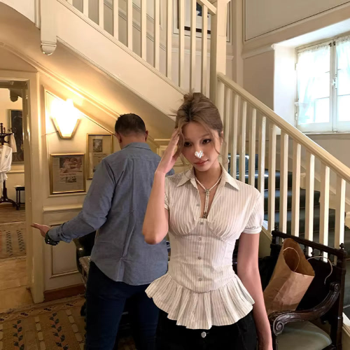 Front view of a light striped blouse with a pointed collar, short puff sleeves, button front, and ruffled peplum hem, worn with black bottoms