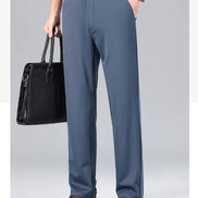 Person wearing gray dress pants with a black leather bag and brown shoes on a light gray background