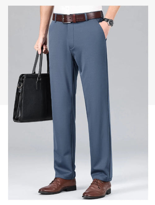 Person wearing gray dress pants with a black leather bag and brown shoes on a light gray background