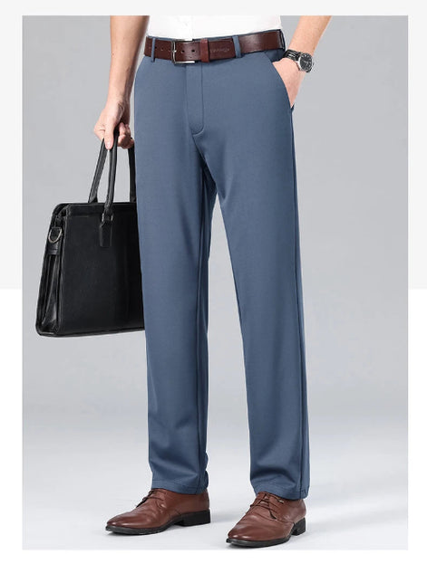 Person wearing gray dress pants with a black leather bag and brown shoes on a light gray background