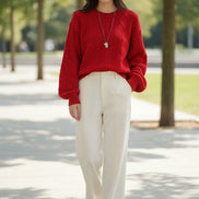 A person wearing a bright red cable-knit sweater with a crew neck and ribbed cuffs, 