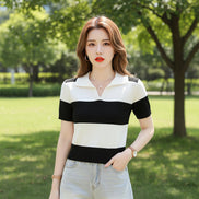 A woman wearing a short-sleeve knit polo shirt with bold black and off-white horizontal stripes, seated on a dark brown leather couch and holding a magazine.