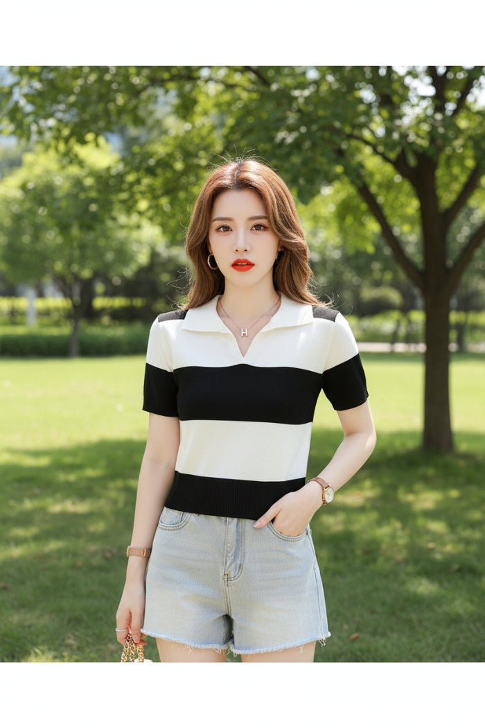 A woman wearing a short-sleeve knit polo shirt with bold black and off-white horizontal stripes, seated on a dark brown leather couch and holding a magazine.