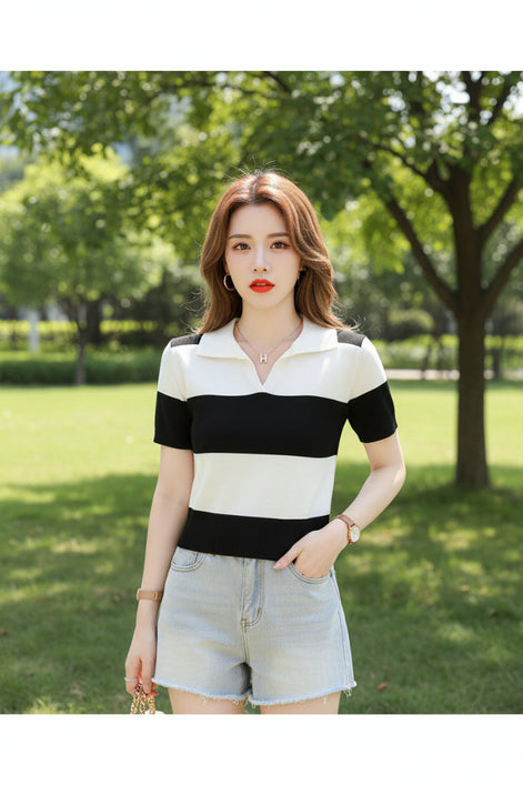 A woman wearing a short-sleeve knit polo shirt with bold black and off-white horizontal stripes, seated on a dark brown leather couch and holding a magazine.