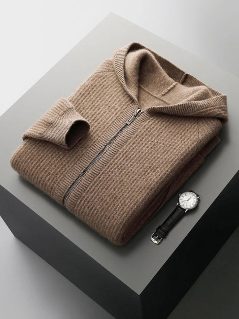 A folded taupe-brown ribbed knit zip-up sweater with a hood, displayed on a dark gray pedestal alongside a black leather strap watch.