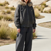Person wearing a dark gray jacket with fur trim and matching pants on a wooden deck.
