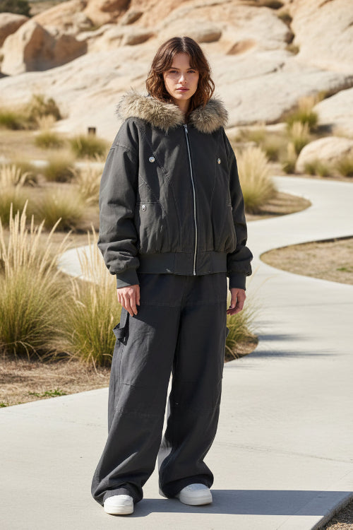 Person wearing a dark gray jacket with fur trim and matching pants on a wooden deck.