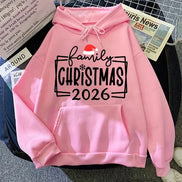A pink pullover hoodie laid flat on a dark surface with newspaper props around it. 