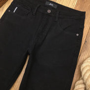 Black denim jeans laid flat on a wooden floor, showing the front waistband, belt loops, button, pocket, and part of the leg.