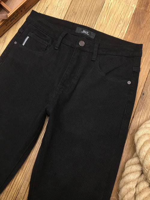 Black denim jeans laid flat on a wooden floor, showing the front waistband, belt loops, button, pocket, and part of the leg.