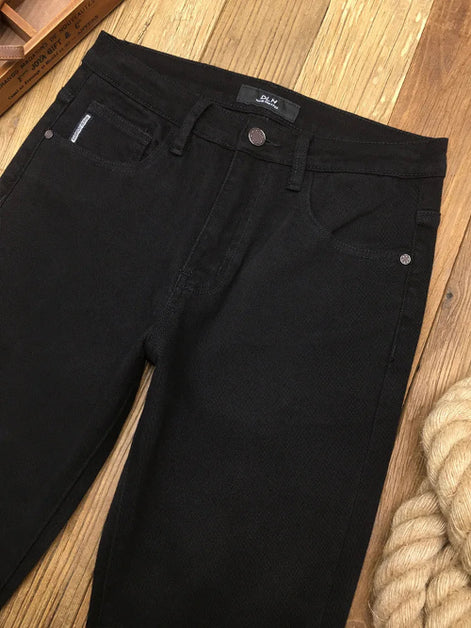 Black denim jeans laid flat on a wooden floor, showing the front waistband, belt loops, button, pocket, and part of the leg.